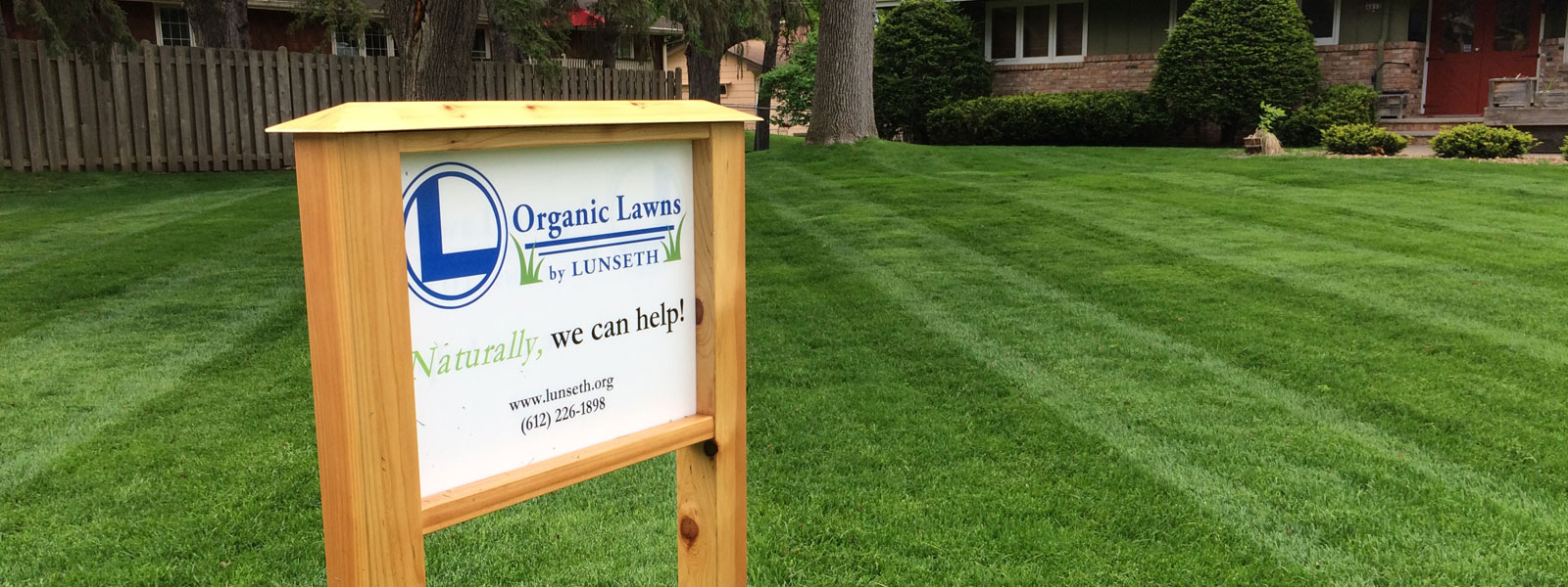 A wooden Organic Lawns by Lunseth sign in a front lawn